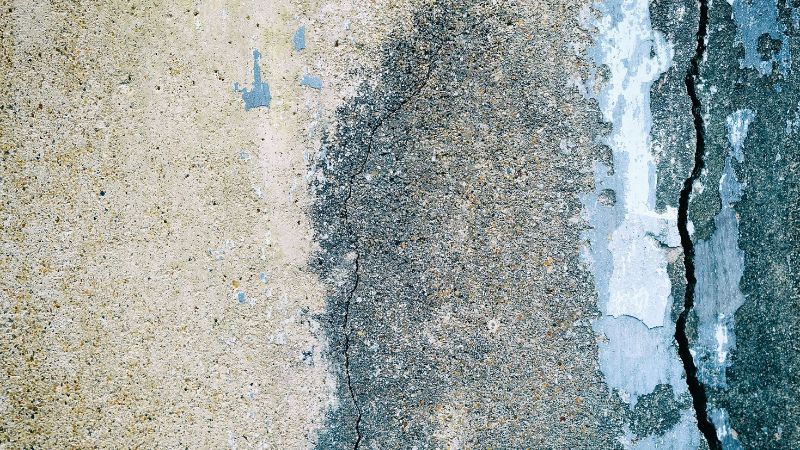 A textured close-up showing the abstract interplay between weathered concrete and asphalt with cracks and peeling layers, highlighting urban decay and the need for painting company intervention to address the passage of time.