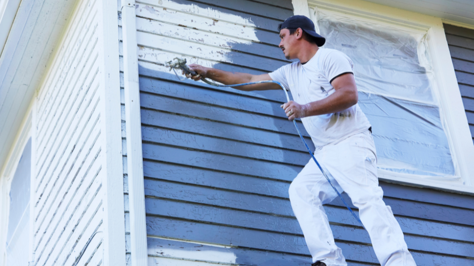 Man pressure washing the exterior of a blue house for a painting company.