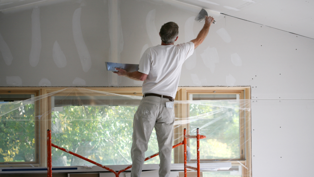 A skilled worker from a painting company meticulously applying joint compound to seams in drywall during a room renovation.