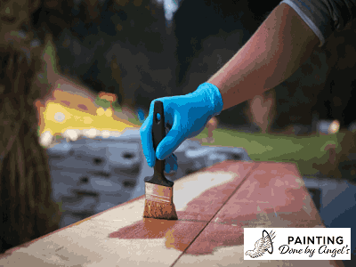 A gloved hand applying stain to a wooden surface, showcasing a step in the process of wood finishing or drywall repair.