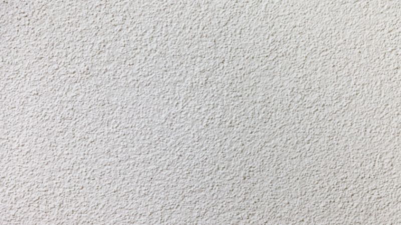 A close-up texture of a white, rough stucco wall with subtle variations in shading.