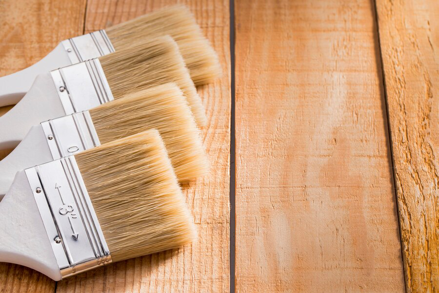 A set of new paintbrushes with wooden handles lined up neatly on a wooden surface, ready for an exterior painting project.