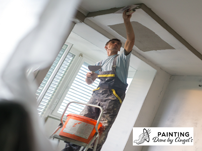 A professional painter from a painting company carefully applying a fresh coat of paint to a ceiling while standing on a ladder.