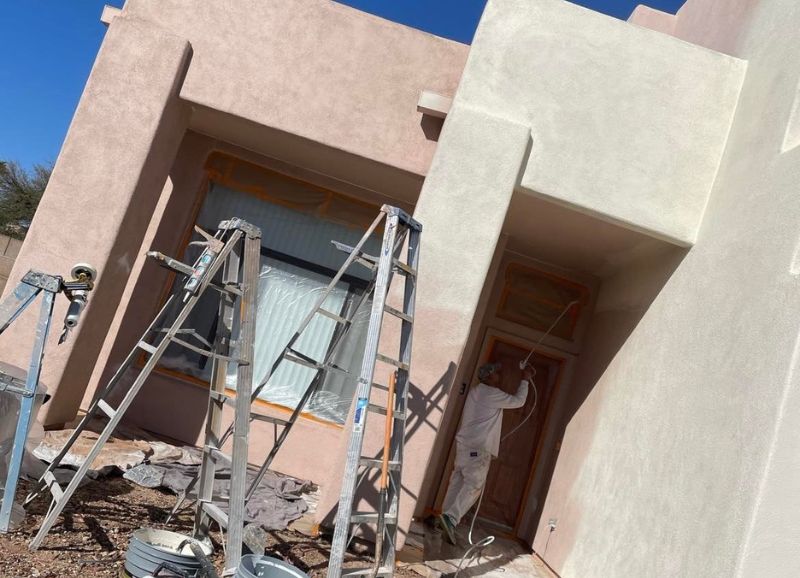 A painter in protective gear works meticulously on a sunny day, with ladders and equipment set up for an exterior painting project.