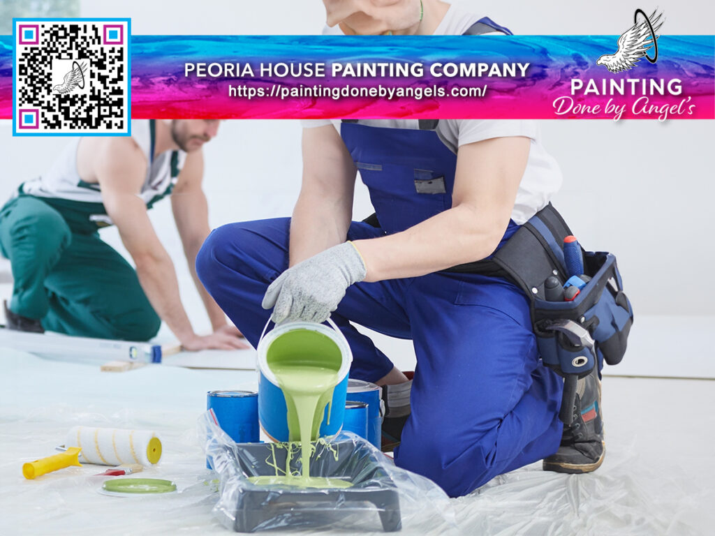 Professional painters from a Peoria house painting company are preparing to paint a room, with one mixing paint colors for interior painting and the other taping the baseboards for neat edges, branding displayed in the