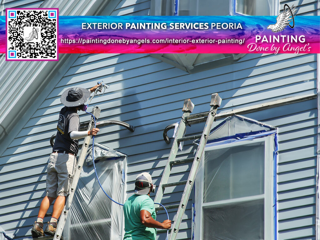 Two professional painters working diligently on the exterior of a blue house, with one on a ladder and the other assisting on the ground, showcasing a day in the life of exterior painting services.