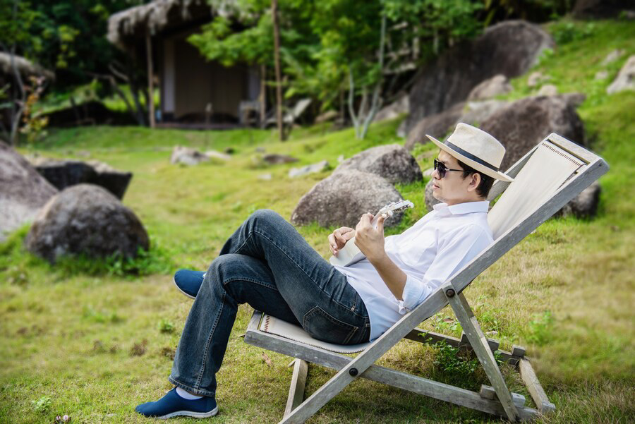 A person relaxing on a lounge chair outdoors, enjoying a book with a serene exterior painting as the backdrop.