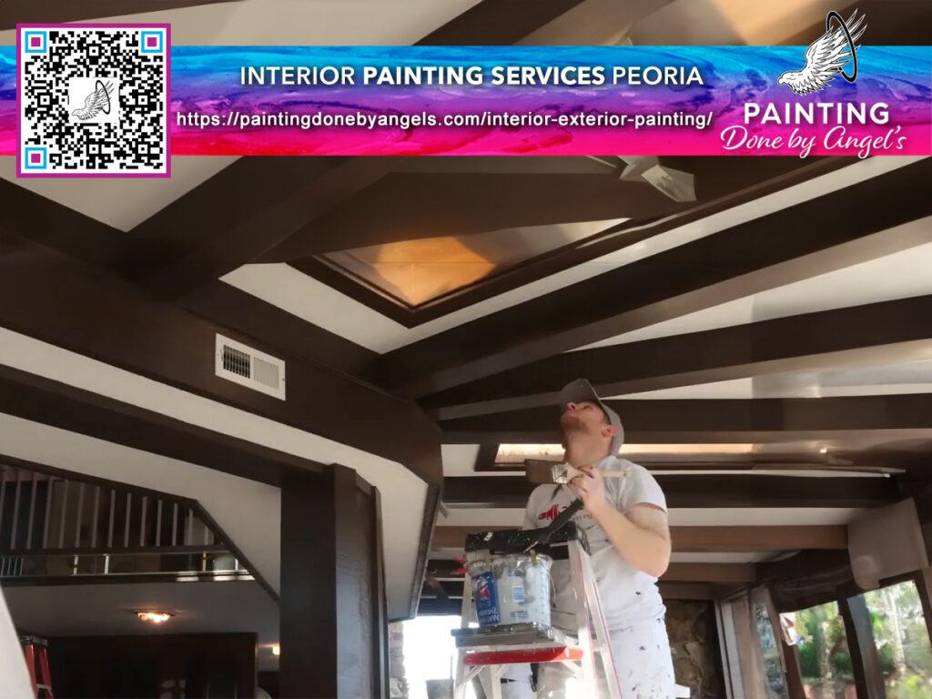 A professional painter on a ladder carefully touching up the edges of a room's ceiling, with a promotional advertisement and QR code for interior painting services by a Painting Company in Peoria displayed prominently in the image