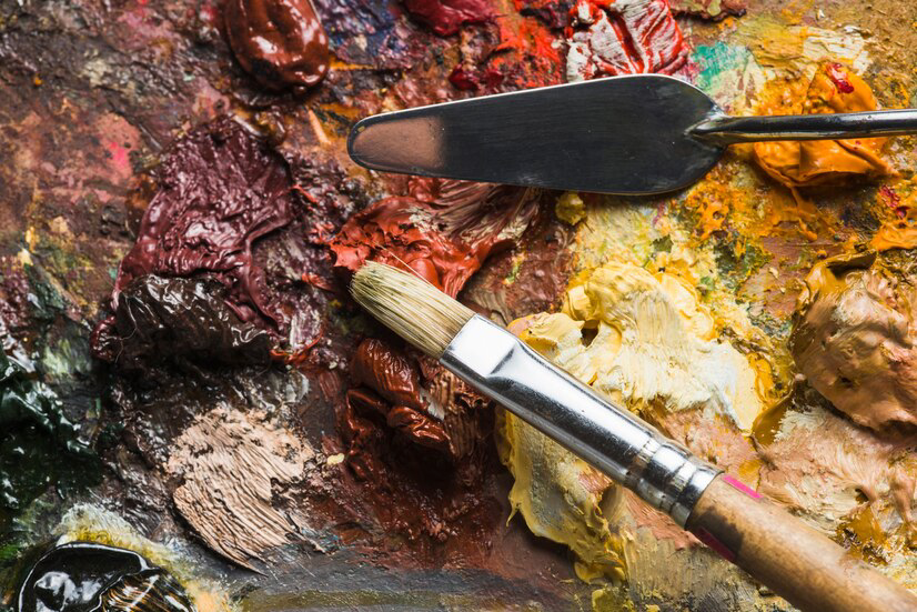 A painting company's palette full of vibrant oil paints and a used paintbrush, with a palette knife lying on top, hinting at a recent session of artistic creation.