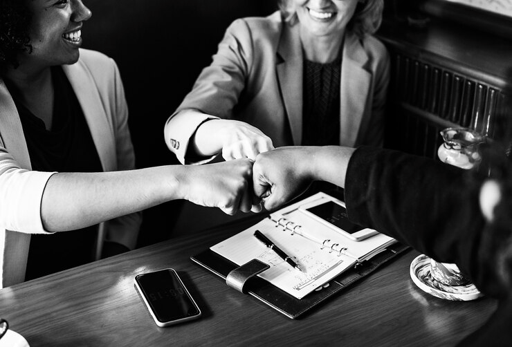 A group of professionals engaging in a cheerful fist bump over a table with smartphones and documents, celebrating collaboration or success in exterior painting.