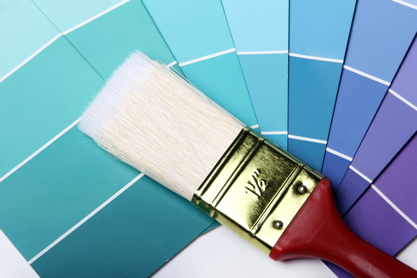 A clean paintbrush rests on a palette of blue to purple paint swatches, symbolizing the beginnings of a home improvement project, specifically painting services, or the selection of colors for an artistic endeavor.