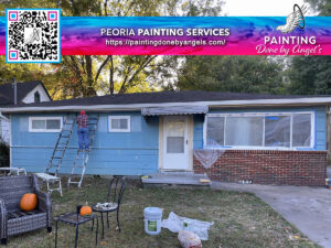 Home renovation in progress with painting services and stucco repair at work, featuring a blue single-story house partially covered with plastic sheeting, a ladder set against the front, and painting supplies scattered on