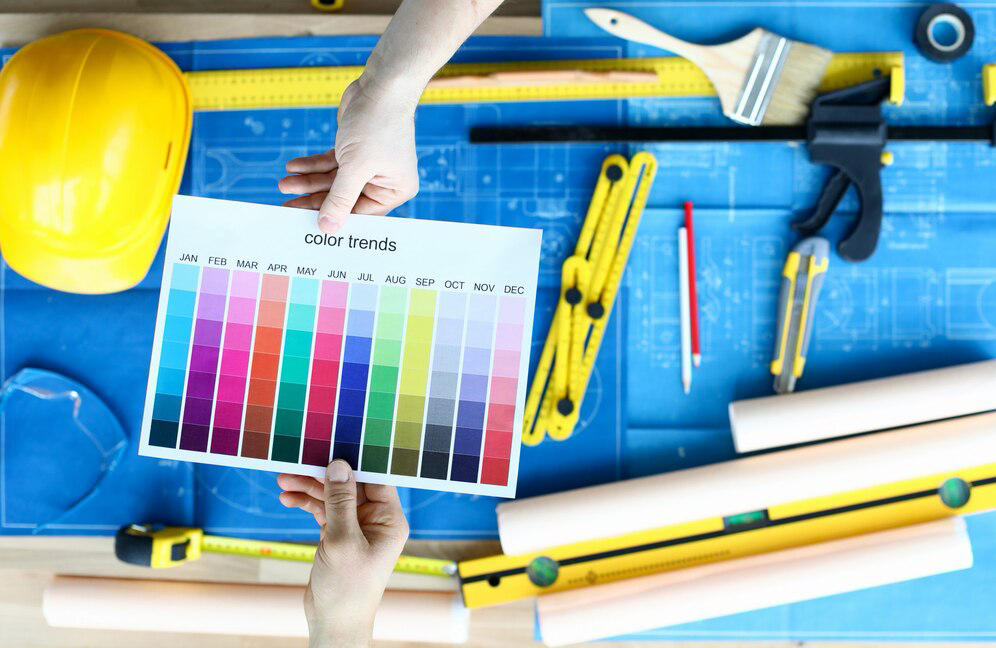 Two individuals collaborating over color trends chart against a background of architectural blueprints and construction tools on a worktable, specializing in Painting Services.