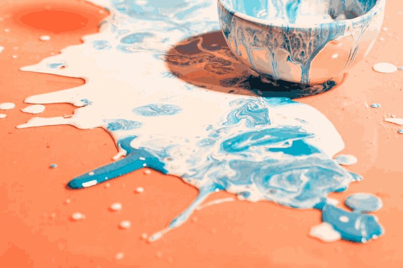 A toppled cup with its contents spilled out on a crimson surface, creating an abstract, marble-like pattern, reminiscent of intricate stucco repair work.