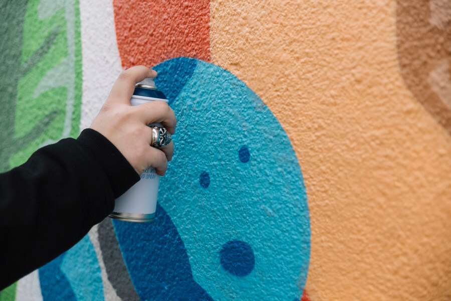 Hand wielding a spray paint can while adding details to a colorful mural for an exterior painting project.