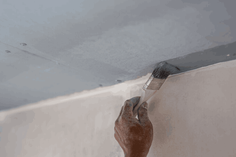 Hand with a paintbrush applying a fresh coat of white paint on an exterior wall.