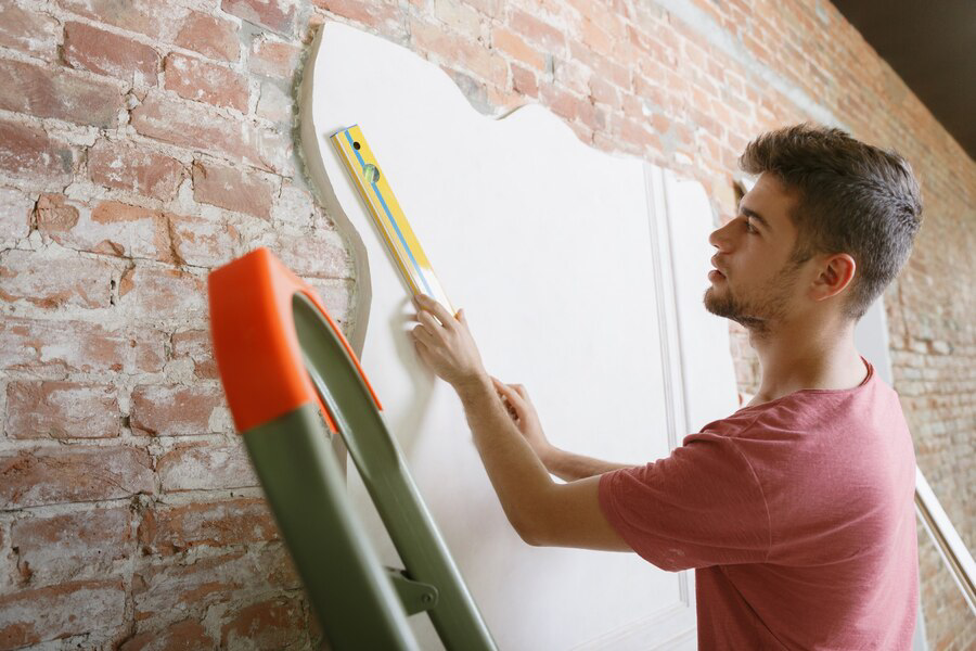 A young man using a level to ensure a straight line as he prepares for interior painting on a brick wall.