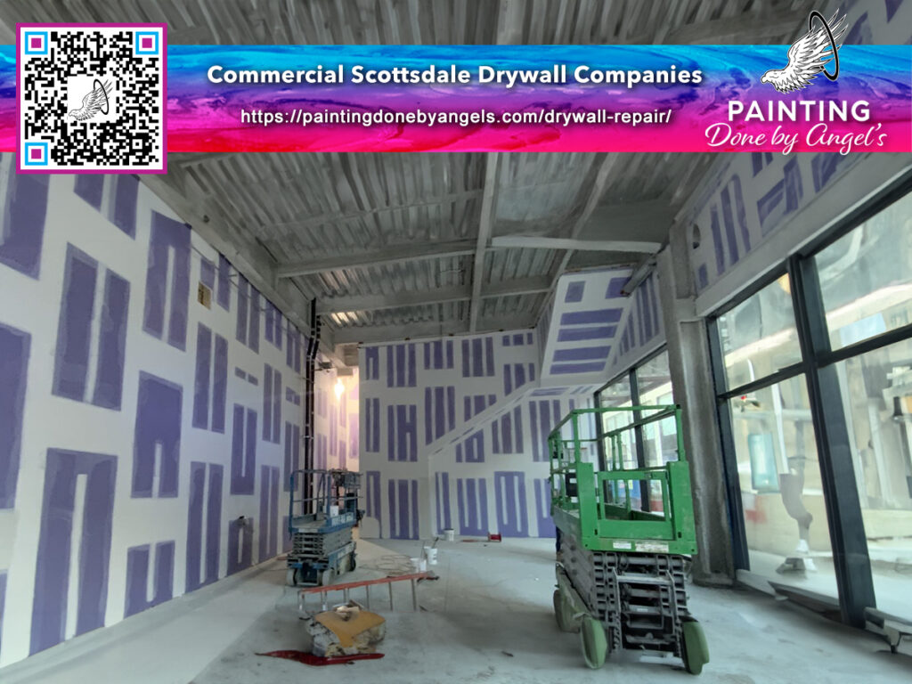Interior construction in progress: drywall installation, stucco repair, and patchwork underway in an empty commercial space, with tools and machinery on site, and a promotional ad for a Scottsdale dry