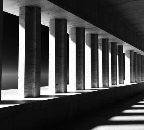Monochrome architectural symmetry: an interior corridor of repeating concrete columns casting stark shadows in a play of light and darkness.