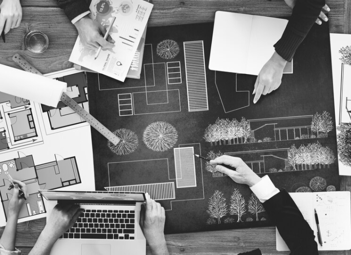 A team of professionals collaborating over an architectural plan with various tools and documents spread out on a table, in preparation for an interior painting project, all captured in a black and white photo.