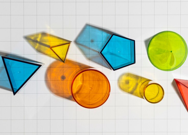 Colorful translucent geometric shapes casting shadows on a grid-lined surface by a painting company.