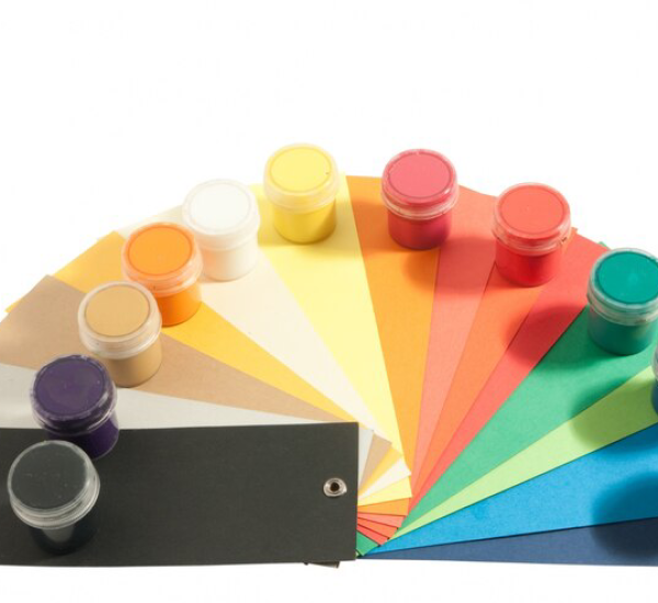 A spectrum of colorful paper samples fanned out beside rows of coordinating paint pots against a white background, symbolizing color matching and selection for interior painting and design projects.